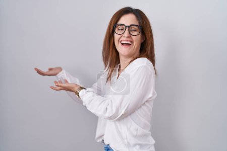 Photo for Brunette woman standing over white isolated background pointing aside with hands open palms showing copy space, presenting advertisement smiling excited happy - Royalty Free Image