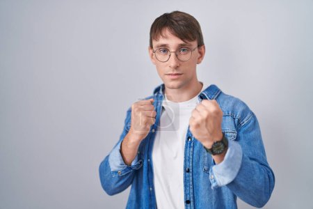 Photo for Caucasian blond man standing wearing glasses ready to fight with fist defense gesture, angry and upset face, afraid of problem - Royalty Free Image