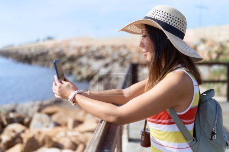 Foto de Joven mujer asiática turista sonriendo confiado usando teléfono inteligente en la playa - Imagen libre de derechos