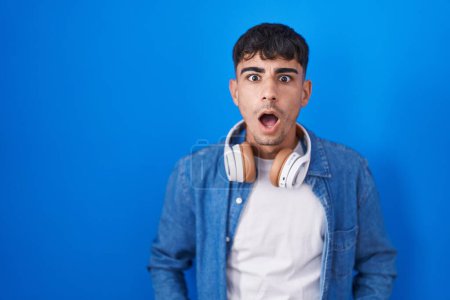 Téléchargez les photos : Young hispanic man standing over blue background afraid and shocked with surprise and amazed expression, fear and excited face. - en image libre de droit