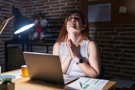 Photo for Brunette woman working at the office at night begging and praying with hands together with hope expression on face very emotional and worried. begging. - Royalty Free Image