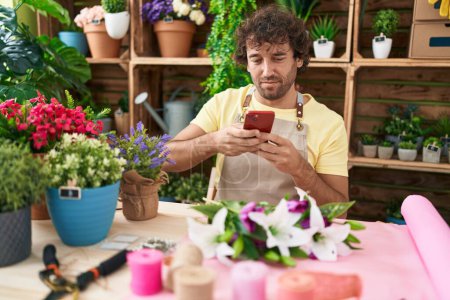Téléchargez les photos : Young hispanic man florist make photo to flowers by smartphone at flower shop - en image libre de droit