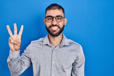 Photo for Middle east man with beard standing over blue background showing and pointing up with fingers number three while smiling confident and happy. - Royalty Free Image