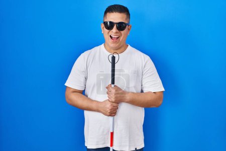 Téléchargez les photos : Hispanique jeune aveugle tenant canne souriant et riant dur à haute voix parce que drôle blague folle. - en image libre de droit