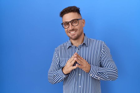 Photo for Hispanic man with beard wearing glasses hands together and fingers crossed smiling relaxed and cheerful. success and optimistic - Royalty Free Image