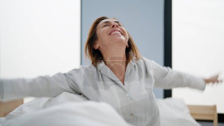 Foto de Mujer hispana de mediana edad despertando con los brazos extendidos en el dormitorio - Imagen libre de derechos