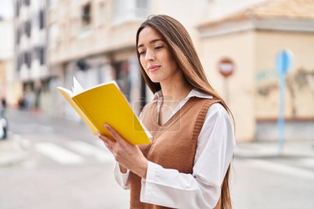 Photo for Young beautiful hispanic woman reading book at street - Royalty Free Image