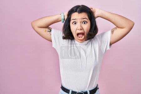 Photo for Young hispanic woman wearing casual white t shirt over pink background crazy and scared with hands on head, afraid and surprised of shock with open mouth - Royalty Free Image