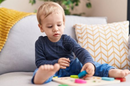 Foto de Adorable niño rubio jugando con las matemáticas juego sentado en el sofá en casa - Imagen libre de derechos