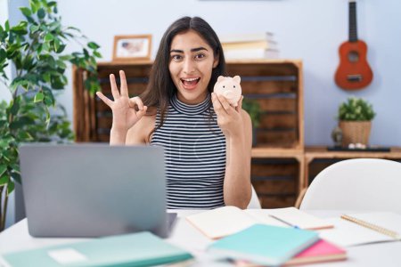 Photo for Young teenager girl studying using computer laptop doing ok sign with fingers, smiling friendly gesturing excellent symbol - Royalty Free Image
