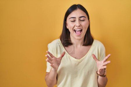 Photo for Hispanic girl wearing casual t shirt over yellow background celebrating mad and crazy for success with arms raised and closed eyes screaming excited. winner concept - Royalty Free Image