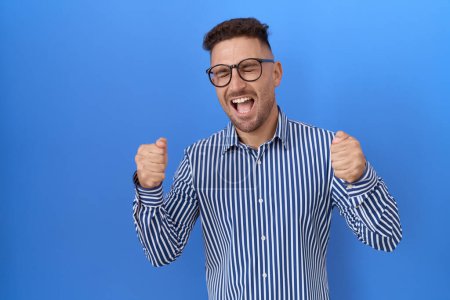 Photo for Hispanic man with beard wearing glasses excited for success with arms raised and eyes closed celebrating victory smiling. winner concept. - Royalty Free Image