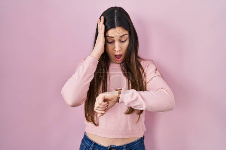 Téléchargez les photos : Young brunette woman standing over pink background looking at the watch time worried, afraid of getting late - en image libre de droit