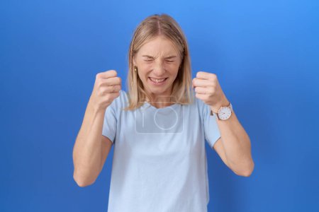 Téléchargez les photos : Jeune femme caucasienne portant un t-shirt bleu décontracté excité pour le succès avec les bras levés et les yeux fermés célébrant la victoire en souriant. concept gagnant. - en image libre de droit