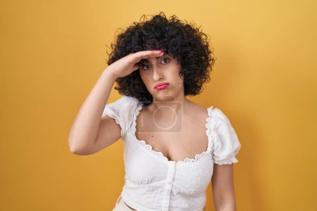 Photo for Young brunette woman with curly hair standing over yellow background worried and stressed about a problem with hand on forehead, nervous and anxious for crisis - Royalty Free Image