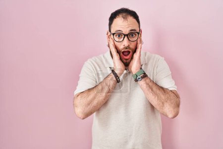 Photo for Plus size hispanic man with beard standing over pink background afraid and shocked, surprise and amazed expression with hands on face - Royalty Free Image