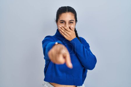 Photo for Young hispanic woman standing over isolated background laughing at you, pointing finger to the camera with hand over mouth, shame expression - Royalty Free Image