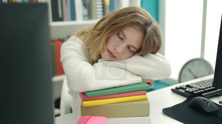 Téléchargez les photos : Jeune étudiante blonde penchée sur des livres dormant à la bibliothèque universitaire - en image libre de droit