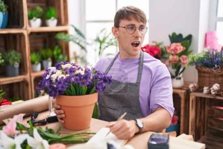 Téléchargez les photos : Homme blond caucasien travaillant au magasin de fleuriste en colère et fou hurlant frustré et furieux, criant de colère. rage et concept agressif. - en image libre de droit
