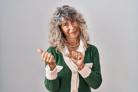 Foto de Mujer de mediana edad de pie sobre fondo blanco apuntando a la espalda con la mano y los pulgares hacia arriba, sonriendo confiado - Imagen libre de derechos