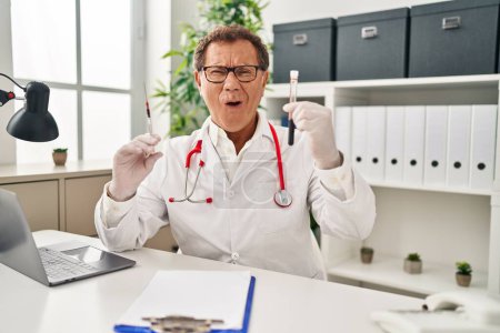 Photo for Senior doctor man holding syringe and blood sample celebrating crazy and amazed for success with open eyes screaming excited. - Royalty Free Image