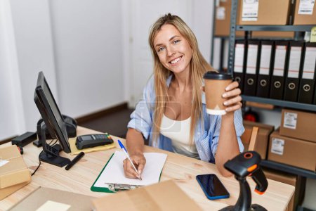 Foto de Young blonde woman ecommerce business worker drinking coffee working at office - Imagen libre de derechos