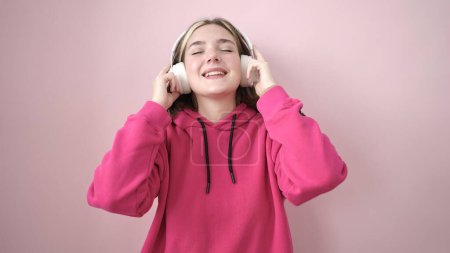 Photo for Young blonde woman listening to music and dancing over isolated pink background - Royalty Free Image