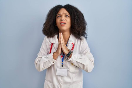 Photo for Young african american woman wearing doctor uniform and stethoscope begging and praying with hands together with hope expression on face very emotional and worried. begging. - Royalty Free Image