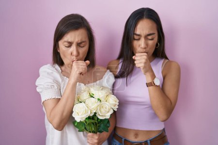 Foto de Madre e hija hispanas sosteniendo ramo de flores blancas sintiéndose mal y tosiendo como síntoma de resfriado o bronquitis. concepto de atención sanitaria. - Imagen libre de derechos