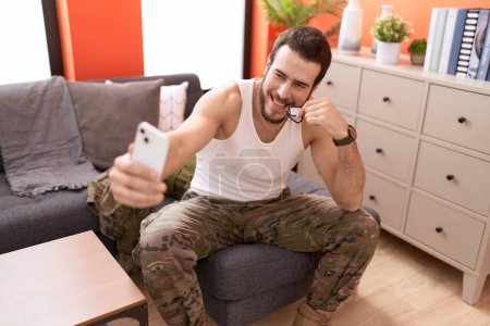 Foto de Joven hombre hispano con uniforme de soldado hacer selfie por teléfono inteligente en casa - Imagen libre de derechos