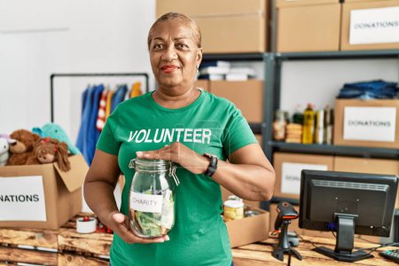 Foto de Mujer afroamericana mayor con uniforme voluntario sosteniendo tarro con dinero en el centro de caridad - Imagen libre de derechos