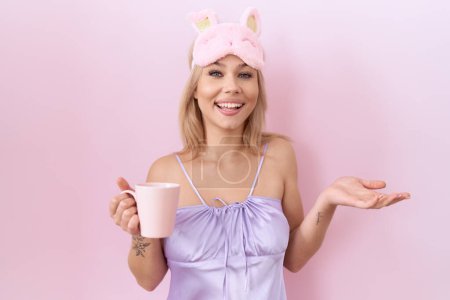 Photo for Young caucasian woman wearing sleep mask drinking a cup of coffee celebrating achievement with happy smile and winner expression with raised hand - Royalty Free Image