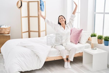 Photo for Young hispanic woman waking up sitting on bed at bedroom - Royalty Free Image