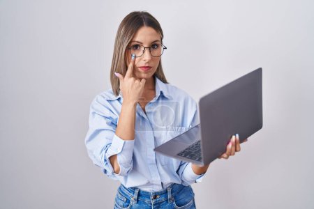 Photo for Young woman working using computer laptop pointing to the eye watching you gesture, suspicious expression - Royalty Free Image