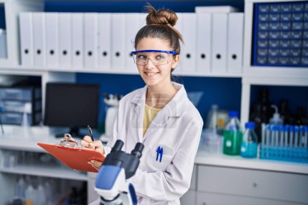 Téléchargez les photos : Adorable girl scientist writing on document working at laboratory - en image libre de droit