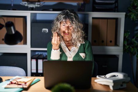 Téléchargez les photos : Femme d'âge moyen travaillant la nuit à l'aide d'un ordinateur portable faisant geste italien avec la main et les doigts expression confiante - en image libre de droit