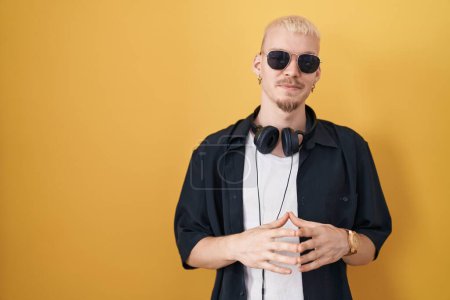 Photo for Young caucasian man wearing sunglasses standing over yellow background hands together and fingers crossed smiling relaxed and cheerful. success and optimistic - Royalty Free Image