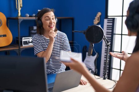 Photo for Two women musicians listening to music composing song at music studio - Royalty Free Image