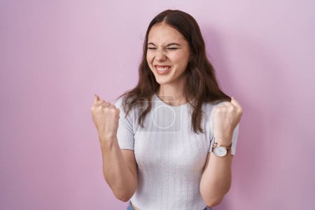 Téléchargez les photos : Jeune fille hispanique debout sur fond rose très heureux et excité faire geste gagnant avec les bras levés, souriant et criant pour le succès. concept de célébration. - en image libre de droit