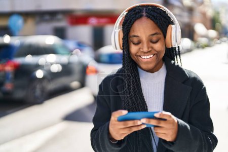 Téléchargez les photos : Afro-américaine femme souriant confiant jouer jeu vidéo à la rue - en image libre de droit