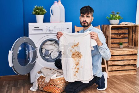 Photo for Young hispanic man with beard holding clean white t shirt and t shirt with dirty stain depressed and worry for distress, crying angry and afraid. sad expression. - Royalty Free Image