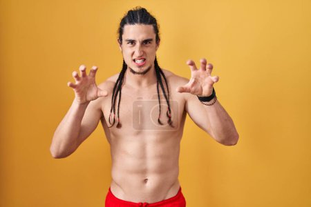 Photo for Hispanic man with long hair standing shirtless over yellow background smiling funny doing claw gesture as cat, aggressive and sexy expression - Royalty Free Image