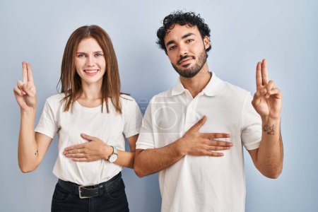 Photo for Young couple wearing casual clothes standing together smiling swearing with hand on chest and fingers up, making a loyalty promise oath - Royalty Free Image