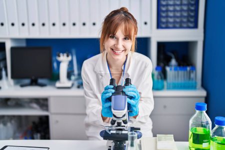 Téléchargez les photos : Young woman scientist smiling confident using microscope at laboratory - en image libre de droit