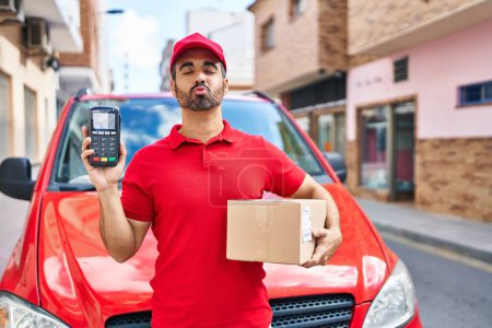 Photo for Young hispanic man with beard wearing delivery uniform and cap holding dataphone looking at the camera blowing a kiss being lovely and sexy. love expression. - Royalty Free Image