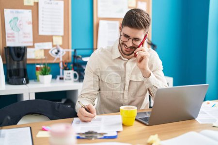 Téléchargez les photos : Young caucasian man business worker talking on smartphone writing on paperwork at office - en image libre de droit