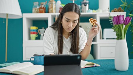 Téléchargez les photos : Jeune belle femme hispanique prenant le petit déjeuner écrivant des notes et utilisant le pavé tactile à la salle à manger - en image libre de droit