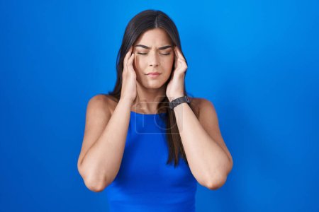 Photo for Hispanic woman standing over blue background with hand on head, headache because stress. suffering migraine. - Royalty Free Image