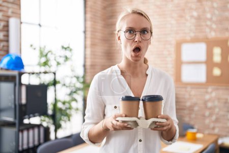 Photo for Young caucasian woman working at the office holding coffee cups afraid and shocked with surprise and amazed expression, fear and excited face. - Royalty Free Image
