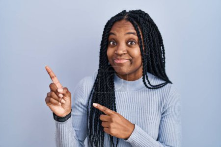 Photo for African american woman standing over blue background pointing aside worried and nervous with both hands, concerned and surprised expression - Royalty Free Image